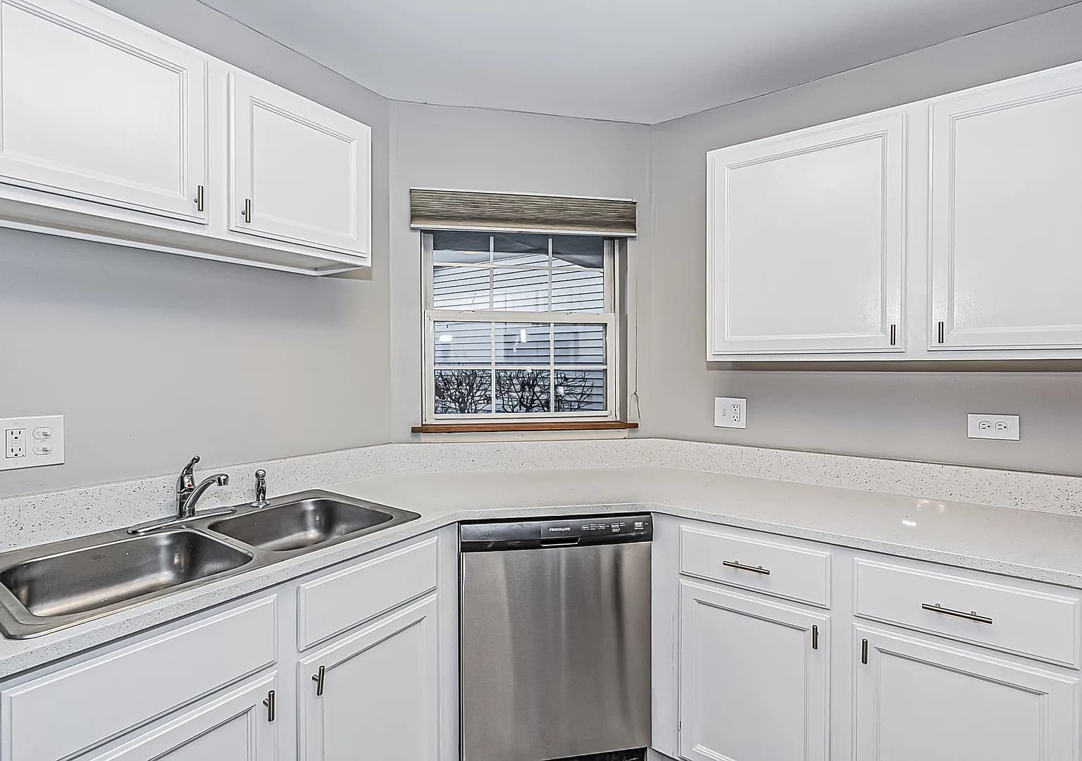Kitchen sink beneath the window with quartz counters and white cabinetry